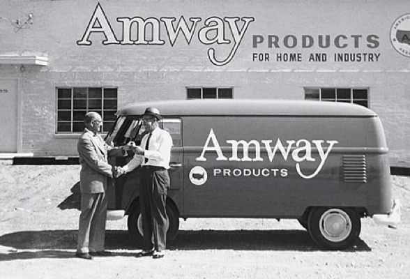 El comienzo de Amway. Foto histórica del edificio de Amway con el texto 'Productos Amway para el hogar y la industria' y de una van de Amway.