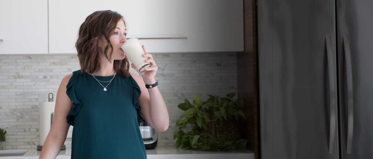 Mujer tomando un batido en la cocina. Logra un estilo de vida con BodyKey, aporta vitaminas, minerales, fibra y proteína.