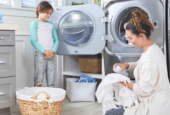 Imagen de una mujer poniendo la ropa a lavar mientras su hija la observa. Elige productos Amway Home para el cuidado de tus prendas.