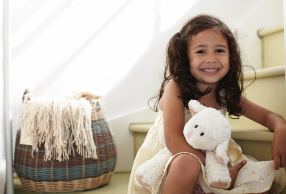 Niña sonriente sentada en una escalera con una cesta de ropa detrás. Los productos Amway Home cumple con las normas del programa Safer Choice de la EPA.