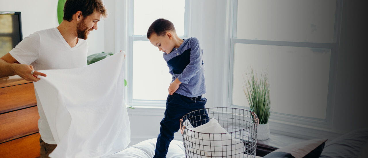 Imagen de un padre e hijo jugando mientras organizan la cama. Elige productos de limpieza Amway Home reconocidos por el Safer Choice de la EPA.